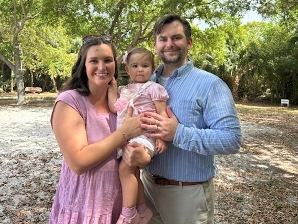 A happy family of three posing outdoors on a sunny day.
