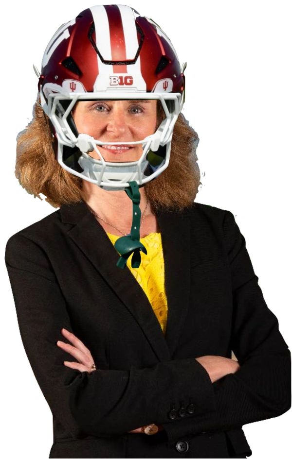 Woman in a business suit wearing a football helmet with a confident smile.