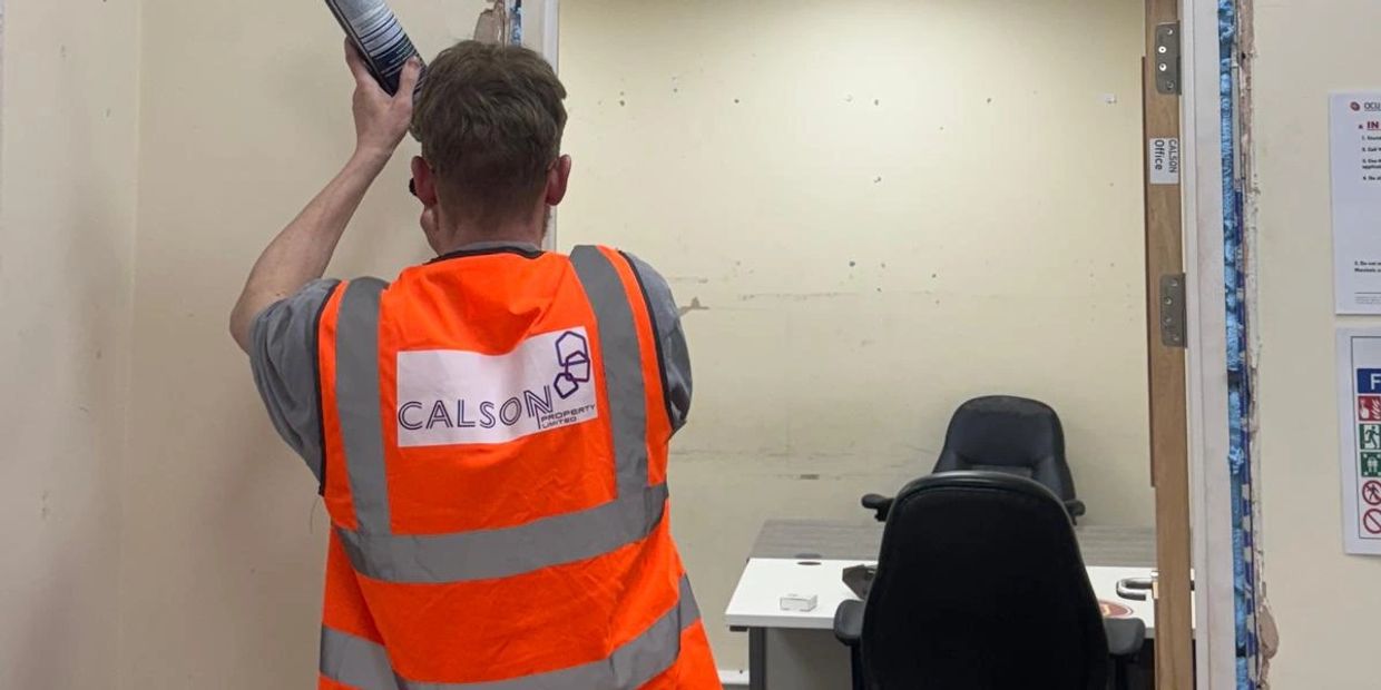 Worker in orange safety vest holding a spray can in an office.