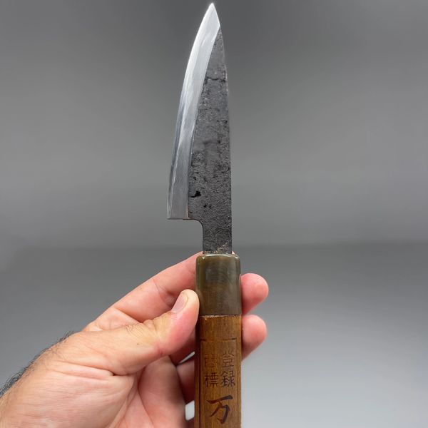 Hand holding a Japanese-style kitchen knife with a wooden handle and engraved characters.