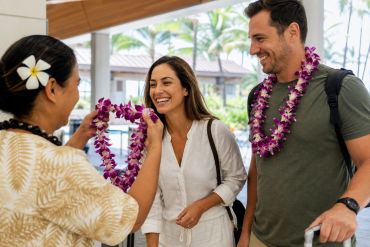 Hawaii lei greeter welcoming an arriving couple with fresh orchid leis at the airport