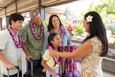 Multi-generational family receiving fresh orchid leis from a Hawaii airport greeter