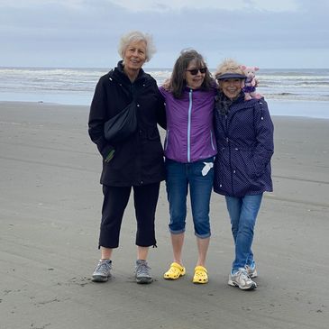 Three women standing together on a beach with the ocean in the background.
