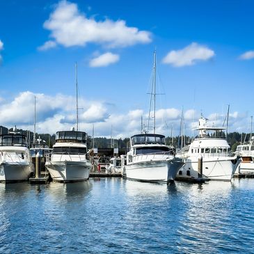 Several white yachts docked in a marina under a partly cloudy blue sky.