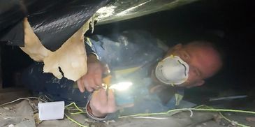 A person wearing a mask and protective clothing inspecting a dark crawl space.