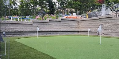 A backyard putting green with three flags and a stone retaining wall.