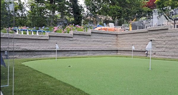 A backyard putting green with three flags and a stone retaining wall.