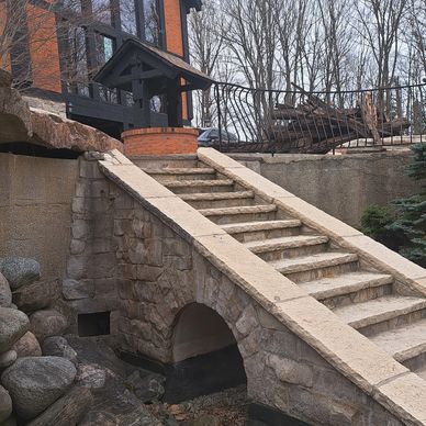 Stone staircase with arch and large windowed house in the background.
