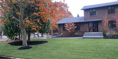 House with autumn trees and fresh green lawn being watered.