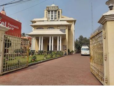 Entrance view of a cream-colored building with columns and a driveway.