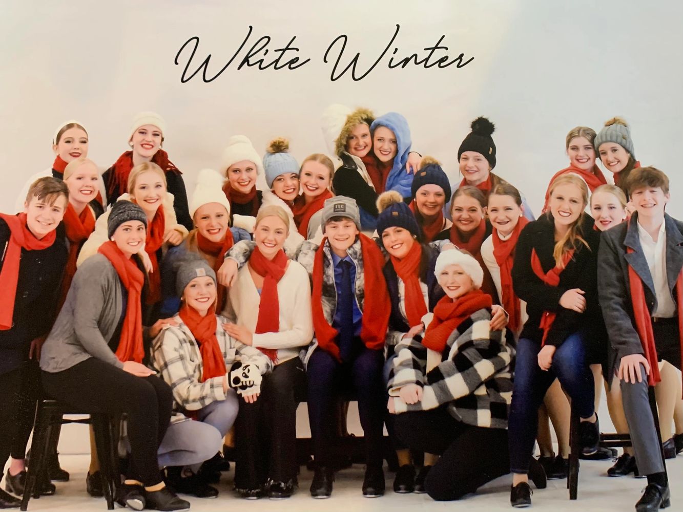Group of young people dressed in winter attire with red scarves posing under 'White Winter' text.