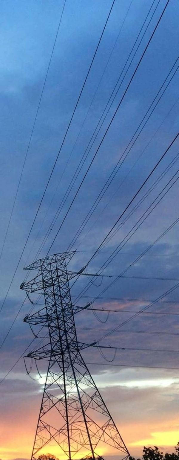 Electric transmission tower silhouetted against a colorful sunset sky.