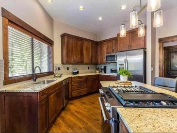 Hanging lights illuminate an oven countertop island in the midst of walnut colored kitchen cabinets