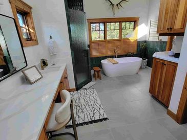 Sun shines through elegant windows upon white tiles and emerald green shower stones of this bathroom