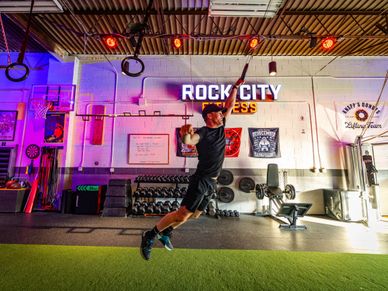 Man jumping in a vibrant gym with 'Rock City Fitness' sign.