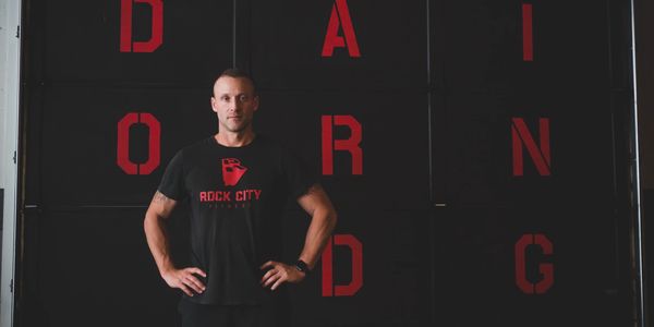 Eric Maust posing in front of the Do Hard Things sign at Rock City Fitness.