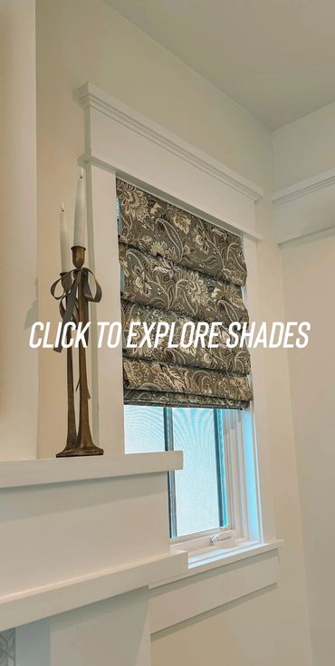 Decorative window with floral Roman shade and tall candle holders.