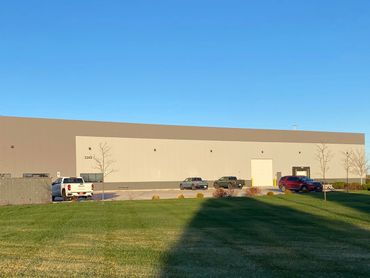 A large industrial building with parked vehicles and green lawn under clear blue sky.