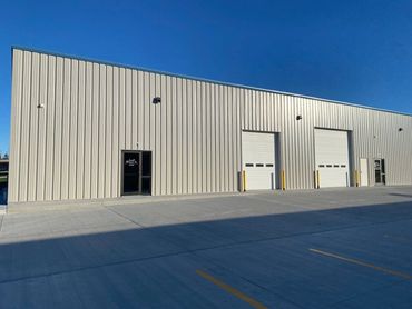 Industrial warehouse with metal siding and two large garage doors under a clear blue sky.