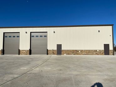 Modern industrial building with large garage doors and two entry doors under a clear blue sky.