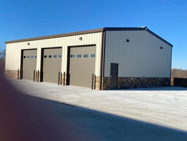 A modern metal garage with three large doors and stone accents under a clear blue sky.