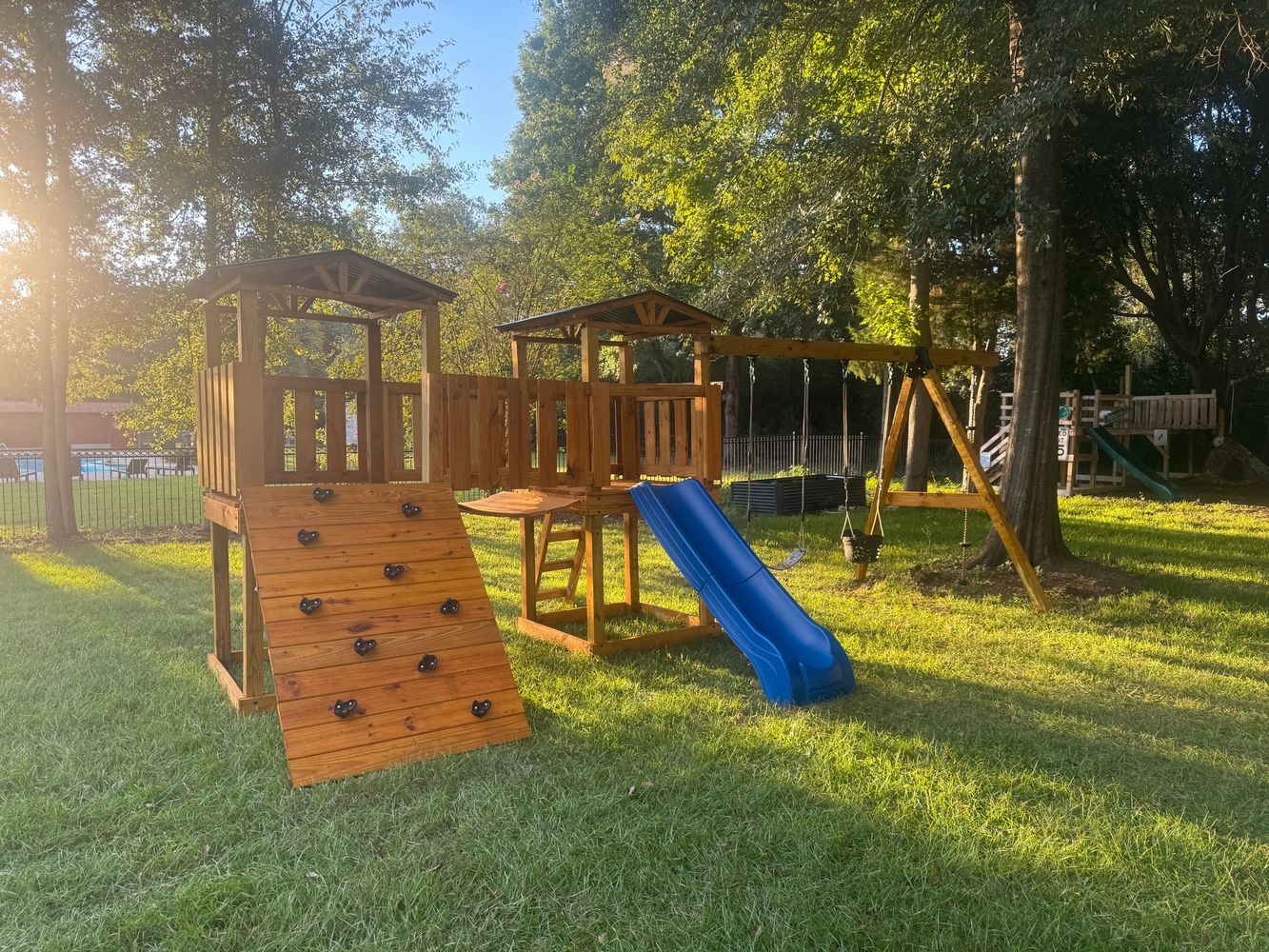 Wooden playground set with slide and swings in a sunny backyard.