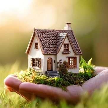 A miniature house model held in a person's hand outdoors.