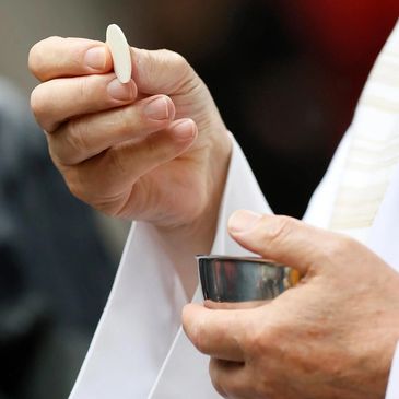 A priest holds a communion wafer and chalice during a religious ceremony.