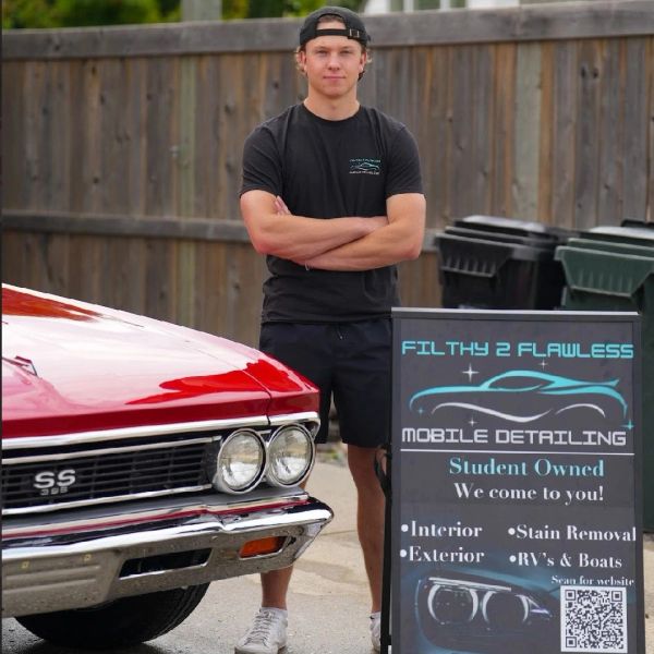 Young man standing beside red classic car and mobile detailing sign.