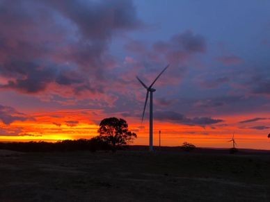 Wind turbines stand against a vibrant sunset sky with scattered clouds.