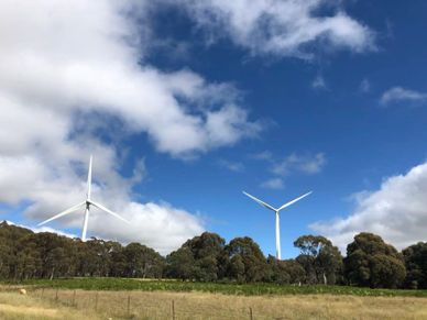 Wind turbines standing tall against a partly cloudy blue sky above green fields.