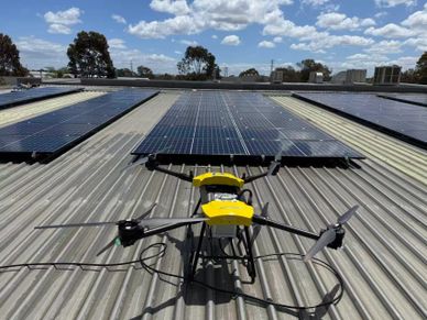 A yellow drone on a rooftop with solar panels under a blue sky.