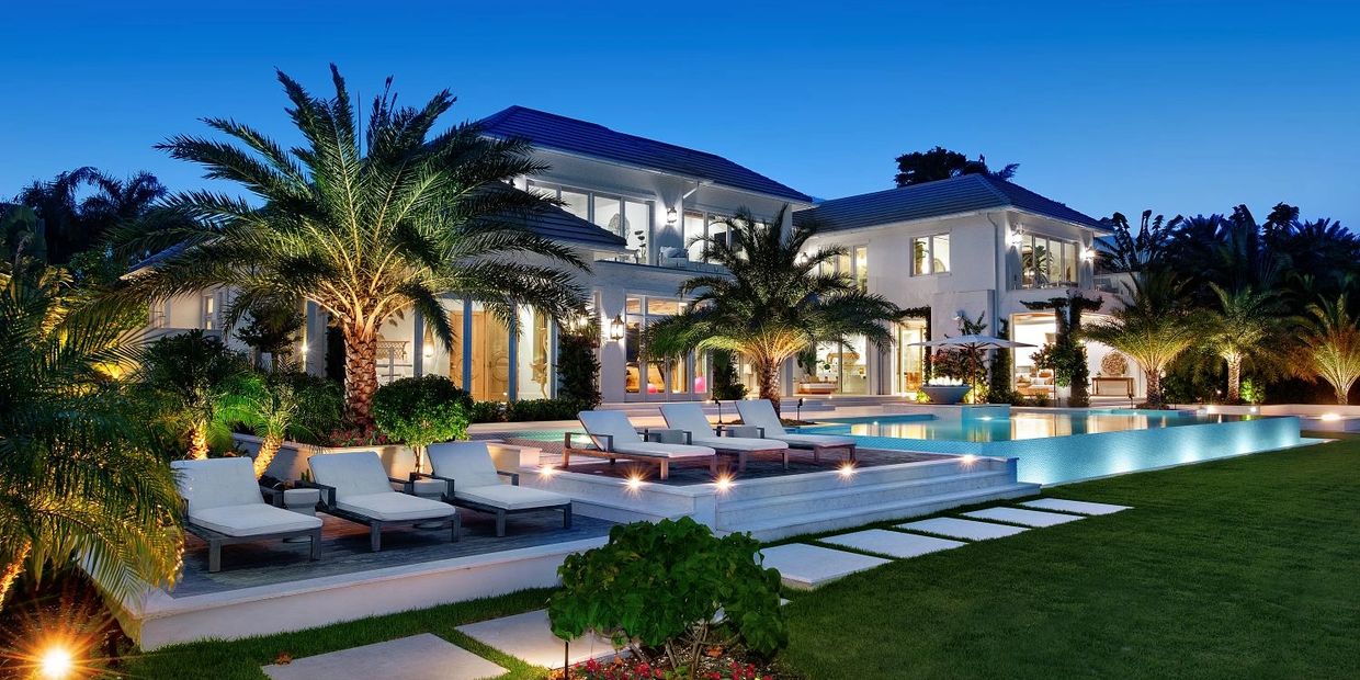 Luxurious modern mansion with illuminated pool and palm trees at twilight.