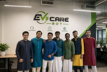 A group of seven men in traditional attire smiling in an office.