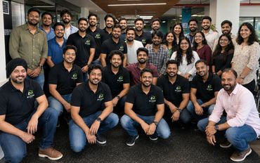 A large group of people posing together indoors, many wearing matching black shirts with a green logo.