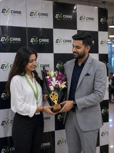 Two colleagues exchanging a bouquet and trophy in front of an EV Care Bot backdrop.