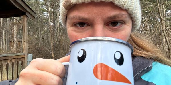 Person drinking from a snowman-themed mug outdoors.