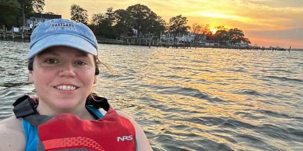 Person smiling by a lake at sunset.