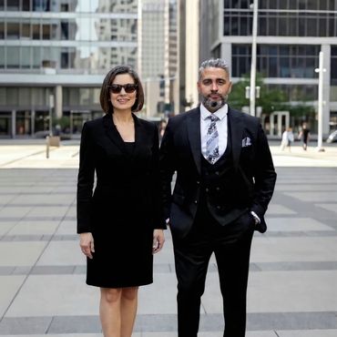 Two professionals in black business attire standing in an urban plaza.