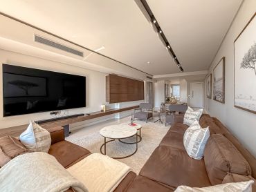 Modern living room with large TV, leather sofas, and round marble tables.