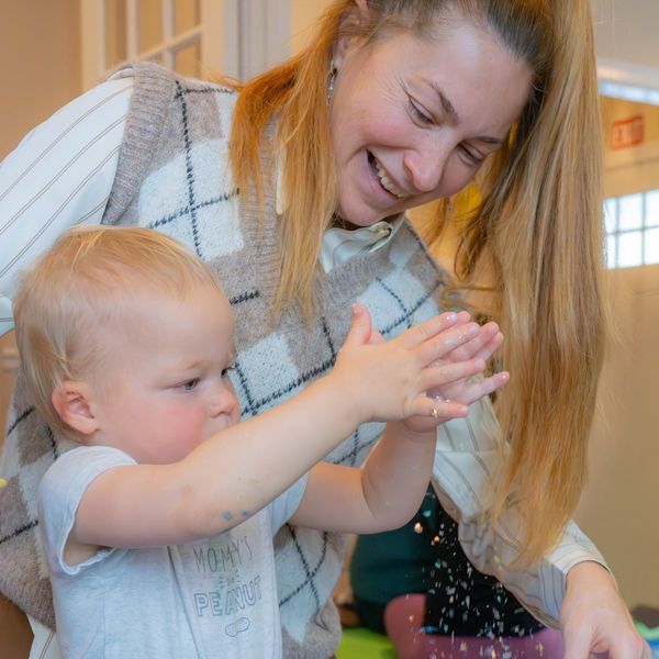 A woman and child joyfully play with sensory materials at a blue table.