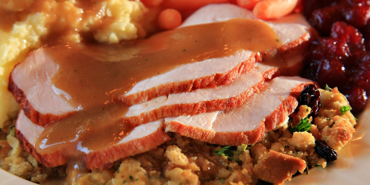 Slices of turkey with gravy over stuffing with cranberry sauce and mashed potatoes.