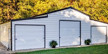 White metal garage with three doors surrounded by greenery.