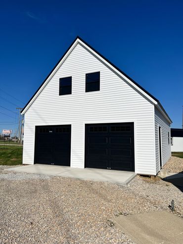 White building with black garage doors under clear blue sky.