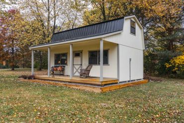 A small white cabin with a porch surrounded by autumn trees.