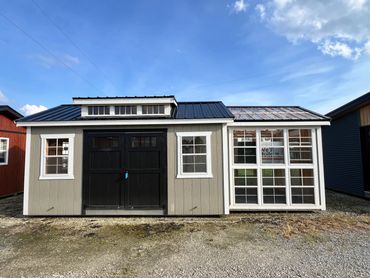 A small gray and white building with black doors and a glass window extension on the right side.