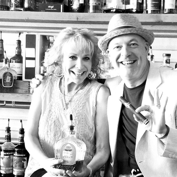 Smiling man and woman at a bar, woman holding a liquor bottle.