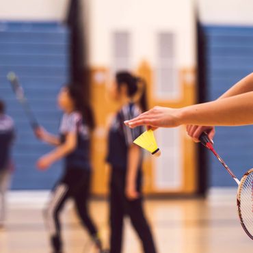 Person holding a shuttlecock and badminton racket in a gym.