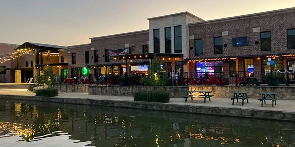 Evening view of a lit restaurant by a calm riverside with outdoor seating.