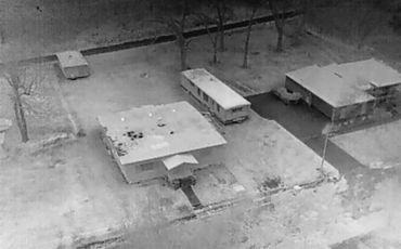 Aerial black-and-white photo of two houses and a trailer in a neighborhood.